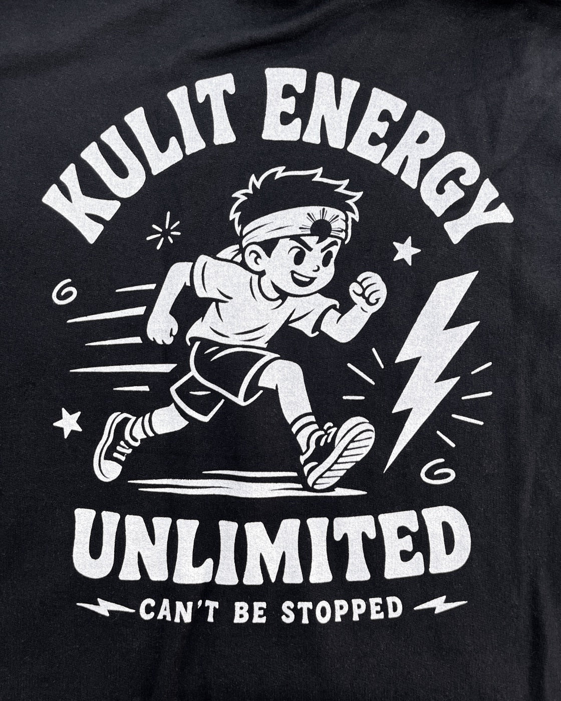 A close-up of a black hoodie featuring a white graphic print of a running cartoon boy with the text 'KULIT ENERGY UNLIMITED' and 'CAN'T BE STOPPED'.