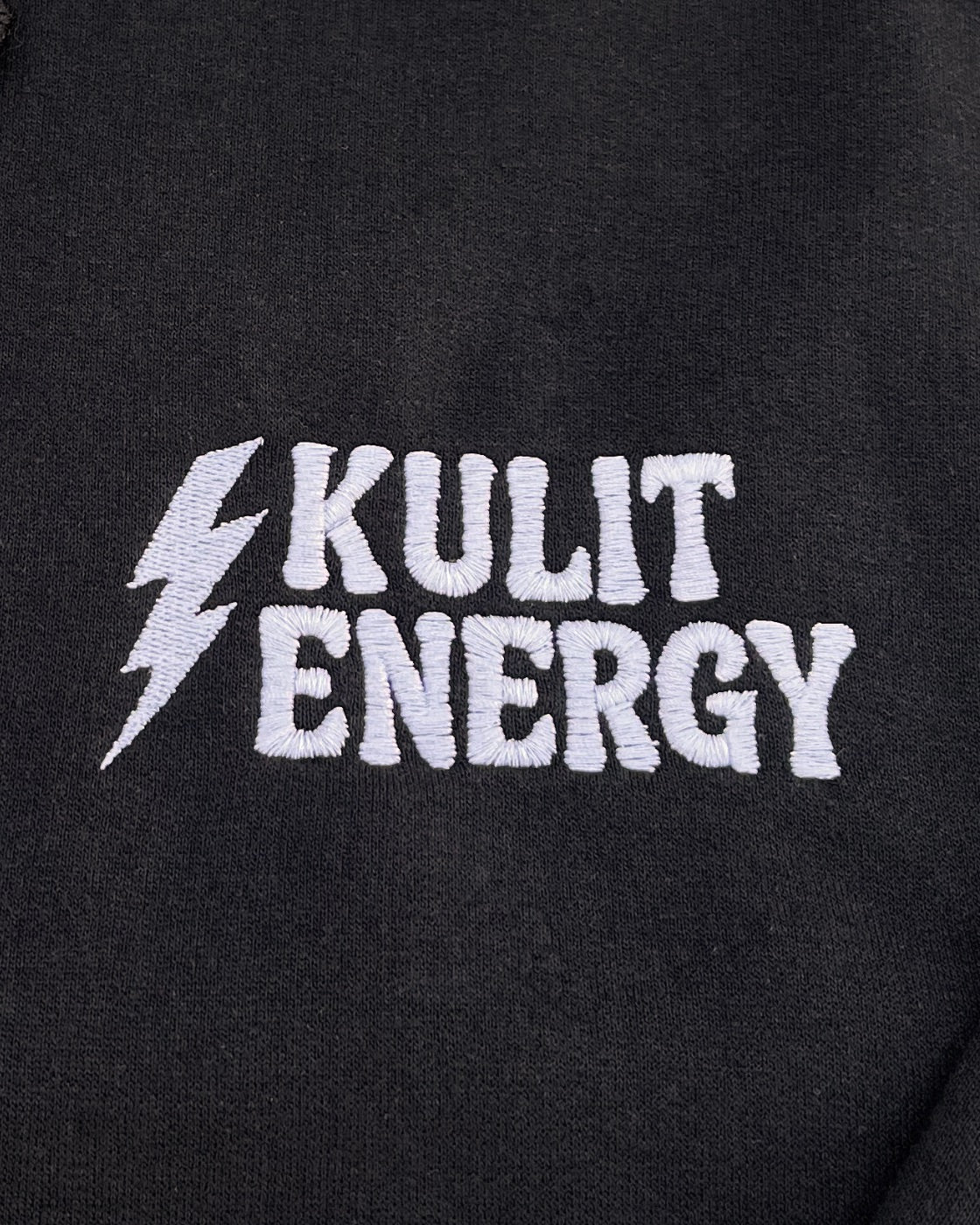 Close-up of a black fabric surface with a large white embroidered logo reading 'KULIT ENERGY' alongside a lightning bolt.