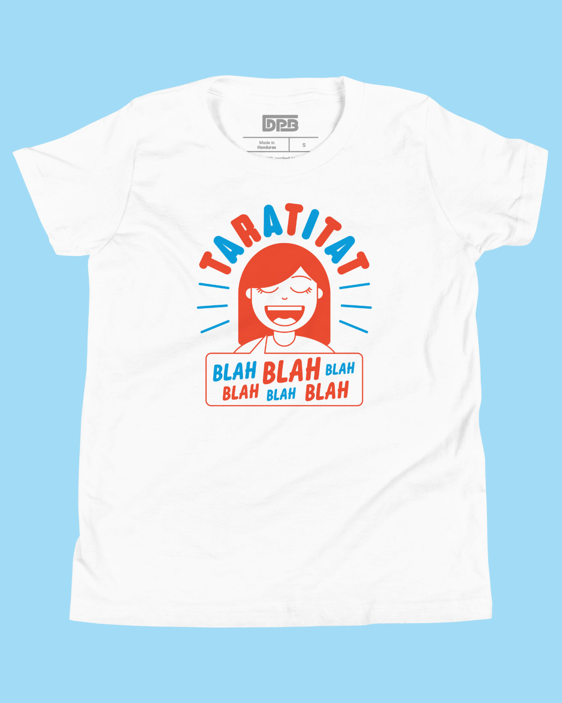 A white short-sleeve graphic t-shirt featuring a cartoon illustration of a smiling girl with red hair and the text 'TARATITAT' and 'BLAH BLAH BLAH' in red and blue, displayed against a solid light blue background.