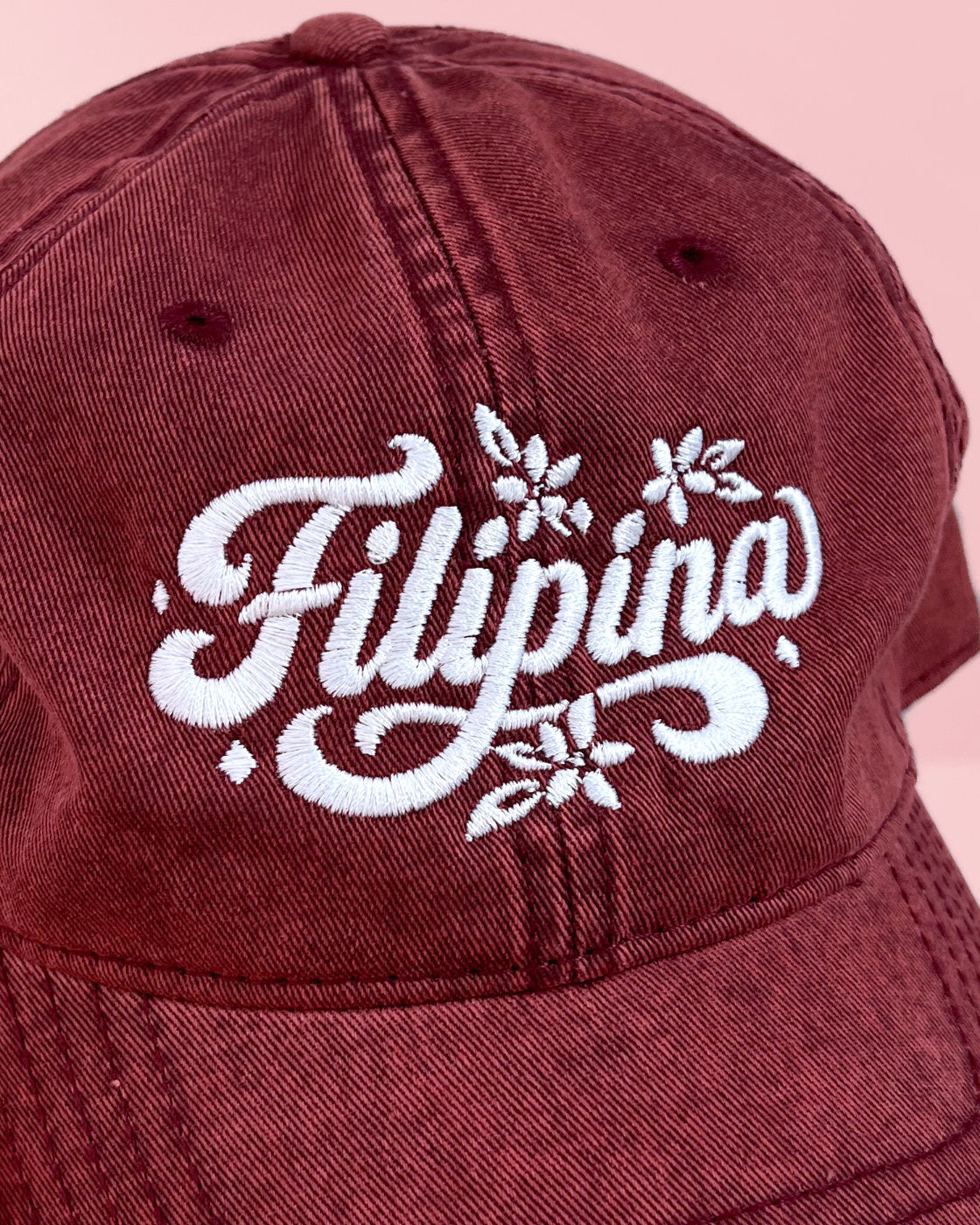 Close-up of white embroidered Filipina lettering and floral design on the front of a maroon vintage cap.