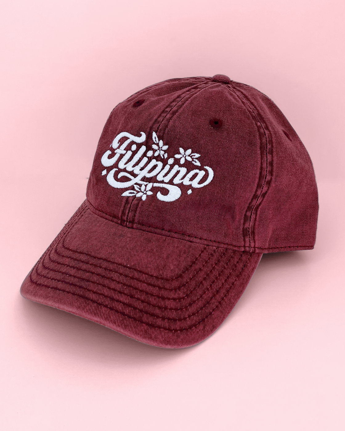 Front three-quarter view of a maroon Filipina vintage cap resting on a flat pink surface.